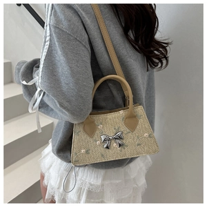 Detail of beige straw handbag featuring floral embroidery and silver bow ornament