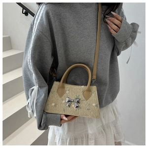 Detail of light beige straw handbag featuring a silver bow and delicate floral embroidery