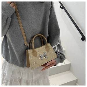 Detail of floral embroidery and silver metal bow on a woven straw-style handbag