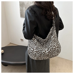 Detailed side view of a large leopard print canvas hobo bag worn with a black leather jacket
