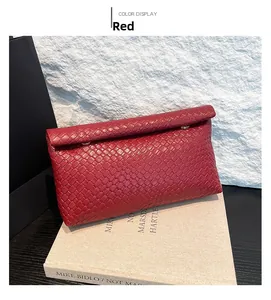 Detail of red woven clutch bag with intrecciato texture leaning on a book