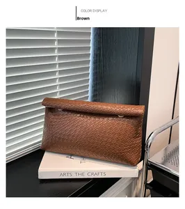 Detail of brown woven PU leather clutch bag with elegant gold rings and fold-over top