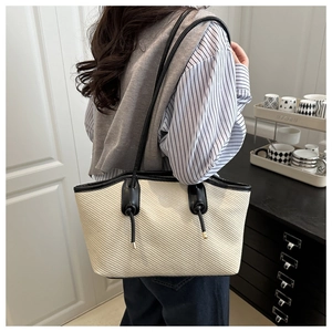 Detail of a beige woven tote bag with black leather trim and long double shoulder straps