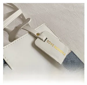 Detail of color-block tote bag showing blue denim, white leather and gold branded tag