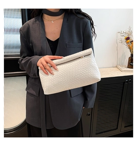 Detail of white woven textured envelope clutch bag held against a grey suit