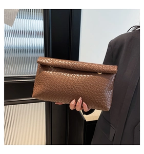Détail de la pochette marron à texture tissée tenue par un mannequin en costume chic