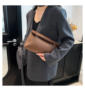 Détail d'une pochette tressée en cuir marron tenue par un mannequin dans un décor épuré