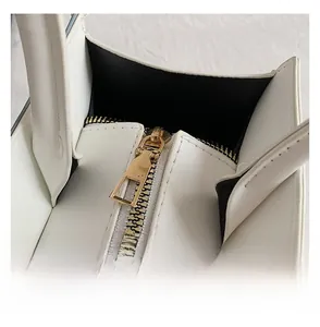 Detailed close-up of white leather handbag featuring smooth gold zipper and stitching