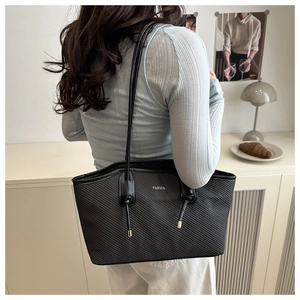 Detail of black textured tote bag with silver FASHION logo and knot handle