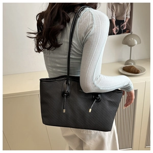 Detail view of black tote bag featuring diagonal embossed texture and gold metal tips