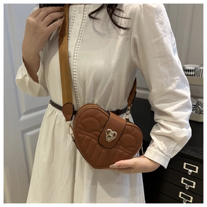 Detail of a brown heart-shaped crossbody bag with quilted pattern and gold heart clasp