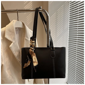 Detail of black leather tote bag with white contrast stitching and decorative silk scarf
