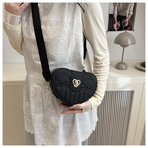 Detail of black heart-shaped quilted bag featuring a gold heart clasp and wide strap