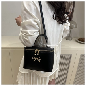 Detail of a black box shoulder bag with golden bow hardware worn by a model in a studio