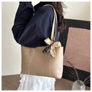 Close-up of beige leather tote bag featuring contrast stitching and floral silk scarf detail