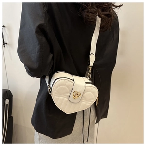 Detail of heart-shaped quilted bag featuring gold heart lock and wide shoulder strap