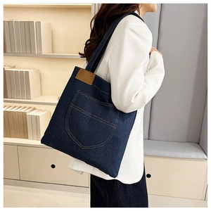 Detail of blue denim tote bag featuring a brown leather patch and stylish front pocket stitching