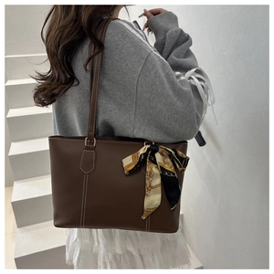 Detail of a brown leather tote bag with white stitching and floral scarf decoration