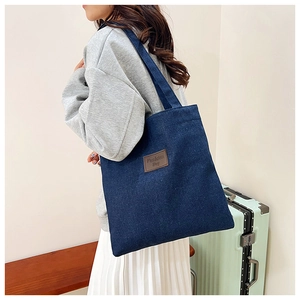 Detail of blue denim tote bag with brown leather patch featuring Fashion Bag text