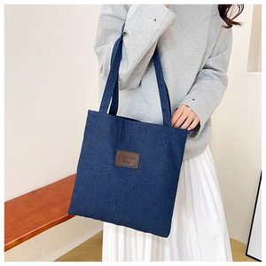 Deep blue denim tote bag with brown leather patch detail shown on female model shoulder