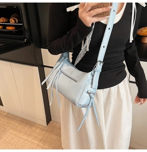 Detalle del bolso de hombro en cuero azul claro con cremalleras de borlas y correa ajustable