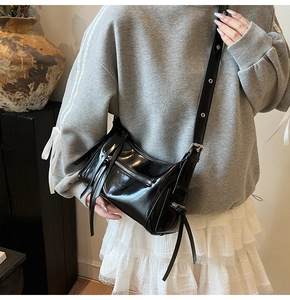 Detalle de bolso bandolera negro brillante con herrajes plateados puesto en un modelo