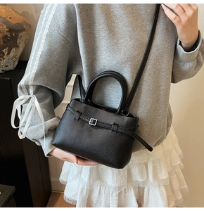 Close-up of a black pebbled leather bucket bag with silver buckle worn by a model