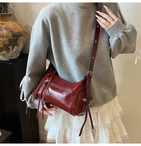 Detalle de bolso de hombro en piel charol granate con flecos largos y cremallera plateada