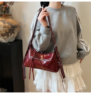 Detalle de bolso de hombro en cuero brillante burdeos con ojales metálicos y flecos