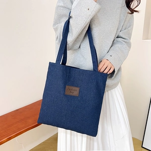 Large blue denim tote bag with leather patch on model in minimalist interior setting