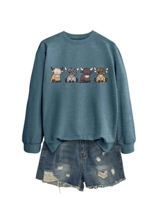 Detail of blue crewneck sweatshirt with four cartoon highland cows and frayed denim shorts