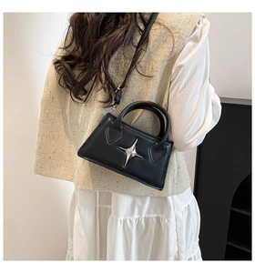 Detail of a structured black crossbody bag with silver star emblem on model back
