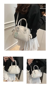 Detail einer cremeweißen Boston Handtasche mit grünem Herzanhänger und weicher PU-Struktur
