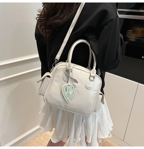 Detail of cream Boston bag with heart charm and textured leather on a model