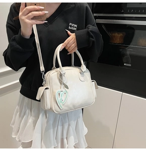 Detail of cream Boston tote bag with side flap pockets and decorative heart pendant