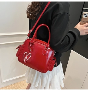 Close-up of a red glossy Boston tote bag with a heart charm shown on a model