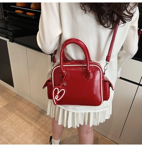 Detail of red glossy Boston tote bag with white piping and heart charm accessory