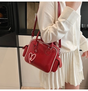 Detail of red patent leather Boston bag featuring heart tag and side flap pocket texture