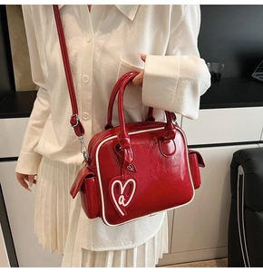 Close-up of bright red patent leather handbag with contrast stitching and heart charm