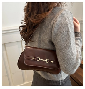 Detail shot of a dark brown leather underarm bag with a golden horsebit buckle on the shoulder