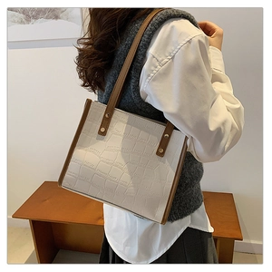 Detail of white crocodile pattern tote bag with brown straps worn by a model