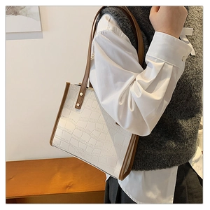 Detail of white crocodile texture tote bag with brown trim and vintage gold rivets