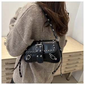 Detail of black leather punk baguette bag with metal studs worn over a beige sweater
