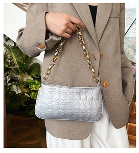 Detail of silver skull embossed handbag with chunky gold chain strap on a model