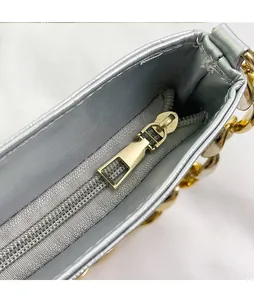 Detailed close-up of metallic zipper and golden chain on silver leather crossbody bag