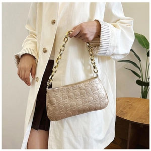 Close-up of golden baguette bag with embossed skull pattern and chunky metal chain