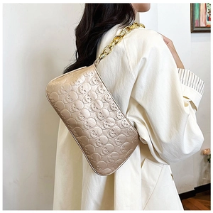 Detail of beige underarm bag with skull embossing and chunky gold chain strap