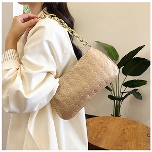 Detail of beige underarm bag with skull embossing and thick gold chain strap