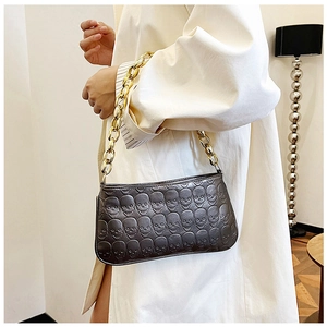 Detail of dark grey handbag with embossed skull patterns and thick gold chain strap