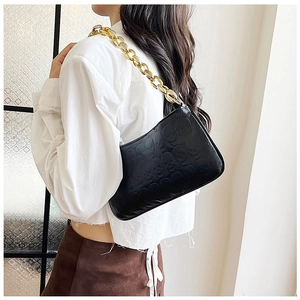 Detail of black punk shoulder bag with skull embossing and gold chain strap on model